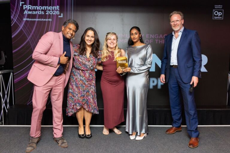Four award winners pose together at the PRmoment Awards 2026, smiling and holding trophy in front of a branded event backdrop.